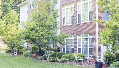 Exterior view of a brick apartment building with a small outdoor seating area and surrounding trees.