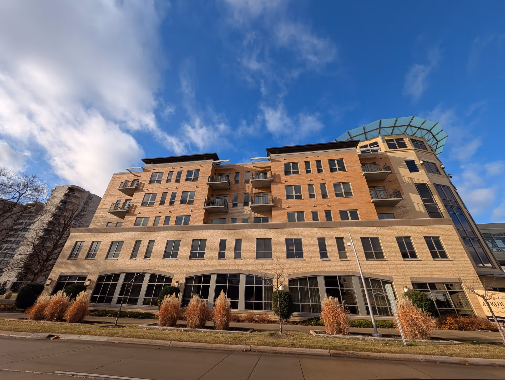 Exterior view of a multi-story senior living facility building named Aurora on France, featuring large windows, balconies, and a modern architectural design under a partly cloudy blue sky.