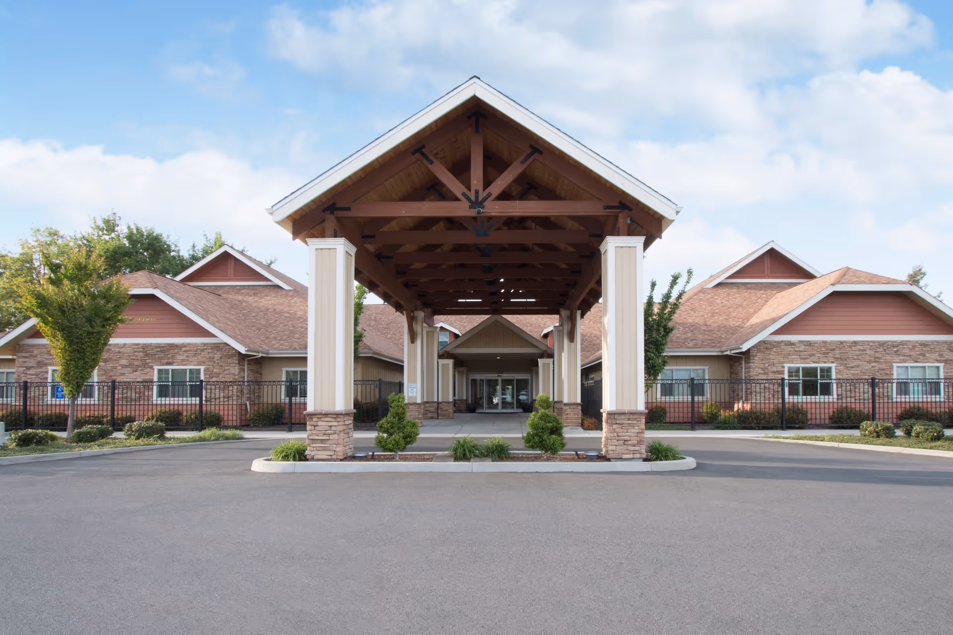 Covered porte-cochère and entrance of a single-story brick-and-siding memory care facility with a landscaped driveway.