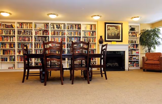Communal library-style living room with a wooden table and chairs in front of a wall of bookshelves and a fireplace.