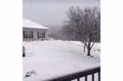 Snowy exterior of a senior living facility with a tree, railing, and distant hills.