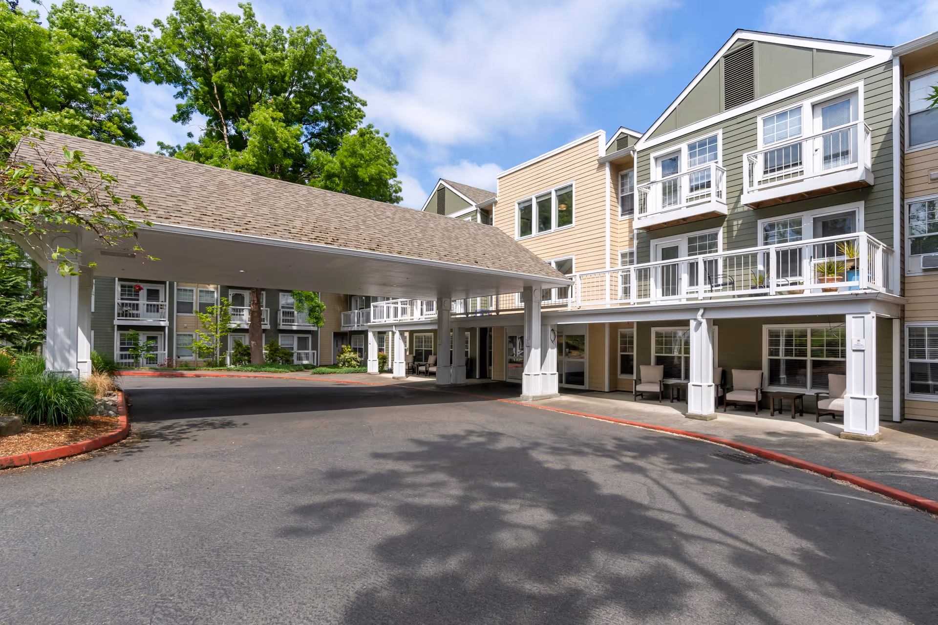 Covered drive-up entrance and front facade of a multi-story senior living building with balconies and outdoor seating.