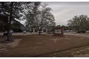 Exterior view of Springdale Health Care Center showing a single-story building with a parking lot in front, surrounded by trees and a grassy area with a sign displaying the facility's name.