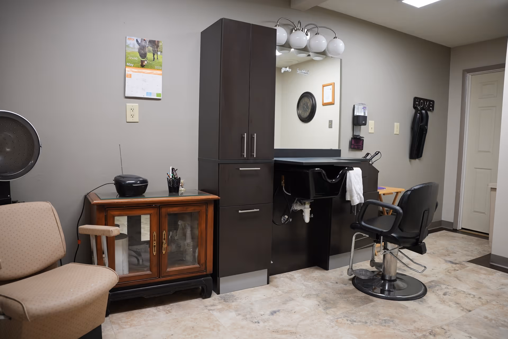 A small salon area with a styling chair, wash basin, tall cabinets, and seating in an interior room.
