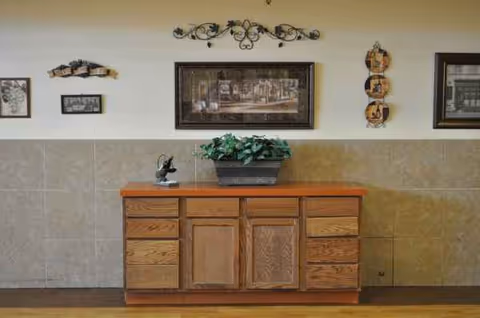 Wooden cabinet with plant and framed art against tiled interior wall.