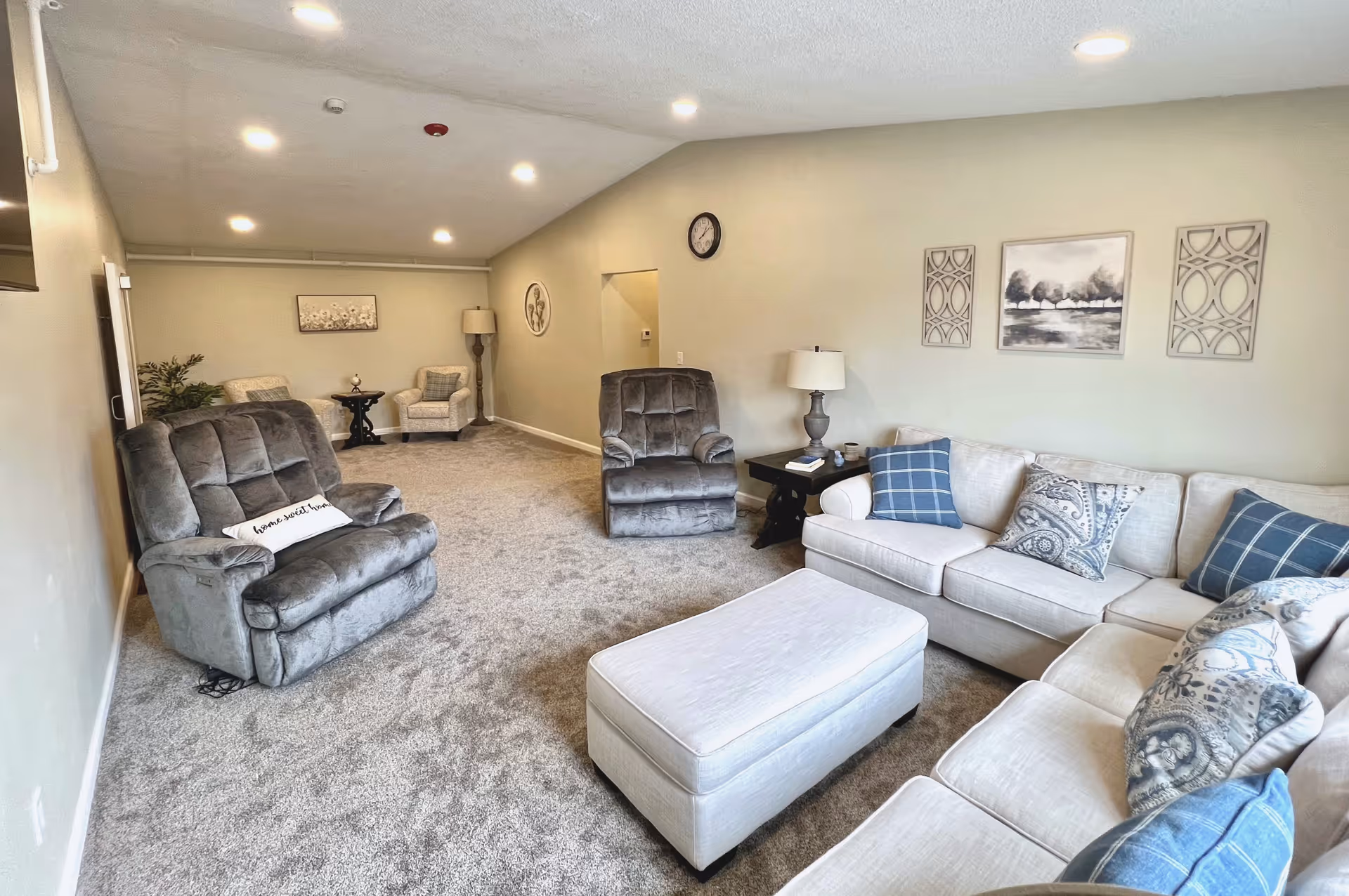Bright furnished living room with a sectional sofa, recliners, ottoman, side tables and wall art.