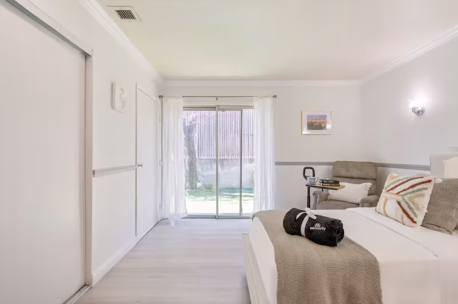 Bright senior living bedroom with bed, chair, and sliding glass door to outdoors.