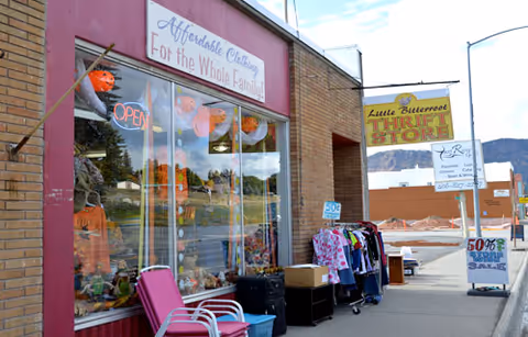 Exterior of a brick building with pink-framed storefront, outside clothes racks, and a Little Bitterroot sign.