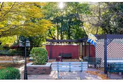 Outdoor garden area with benches, a brick planter, a lamppost, and a lattice fence. Trees with green and yellow leaves provide shade in the background.
