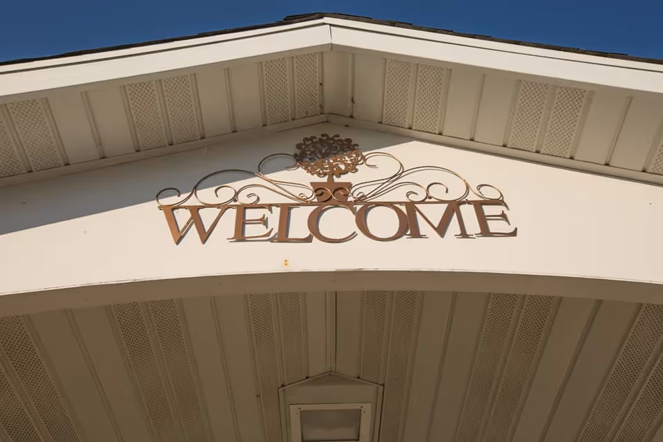 A decorative metal sign with the word 'WELCOME' mounted on the exterior of a building under the roof eaves.