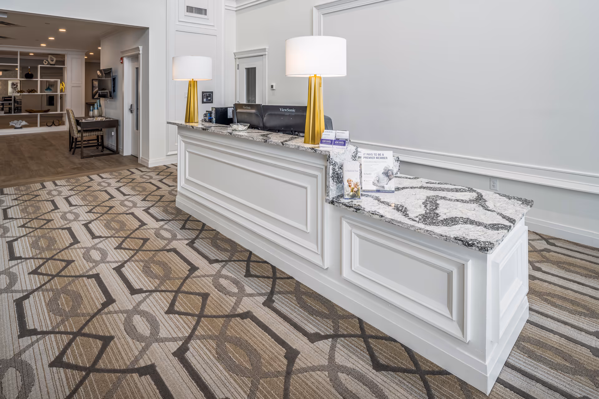 Reception desk and lobby area with a marble countertop, two table lamps and patterned carpet.