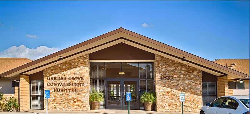 Front entrance of Garden Grove Convalescent Hospital with a stone façade, glass doors, potted plants, and a pitched roof.