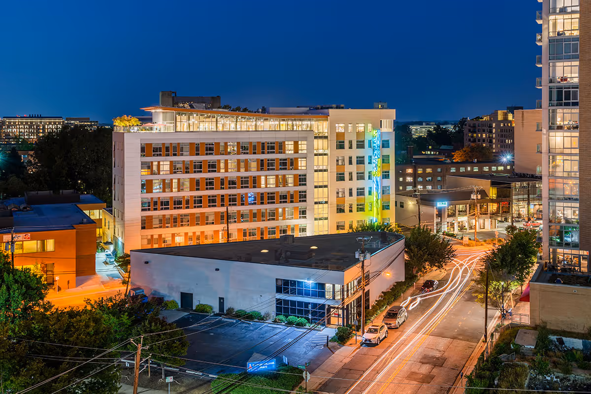 Nighttime view of the Modena Reserve Bethesda multi-story residential building illuminated above a city street with car light trails.