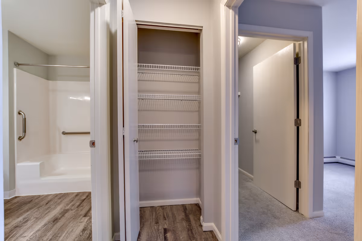 Hallway closet with wire shelving between a bathroom with a tub/shower and an open bedroom doorway.