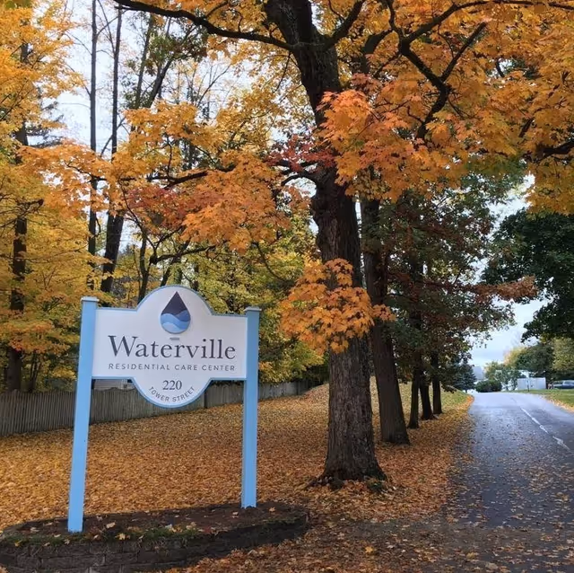 Entrance sign for Waterville Residential Care Center beside a tree-lined road covered in autumn leaves.