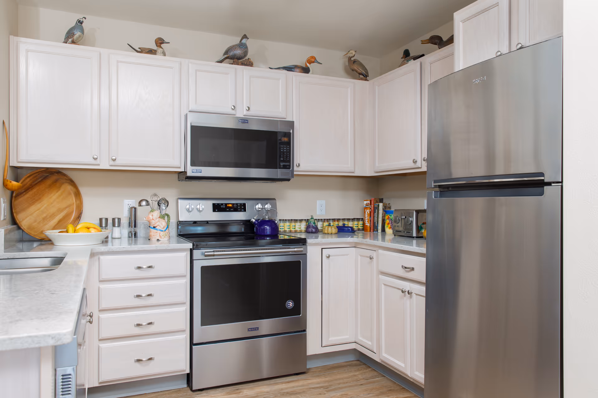 A modern kitchen with stainless steel appliances, light wood cabinets, and decorative duck figurines displayed above the cabinets.
