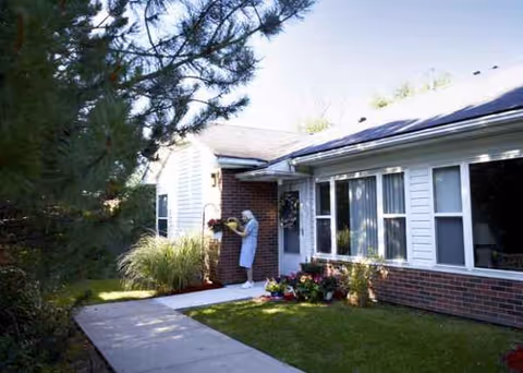 A person stands by the front entrance of a single-story senior living building outdoors.