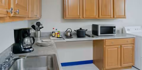 Compact kitchen with wooden cabinets, sink, microwave, coffee maker, and utensils.