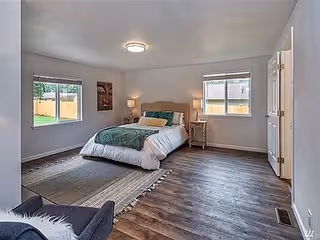 Spacious bedroom with a bed centered between two windows, hardwood floors, area rug and bedside tables.