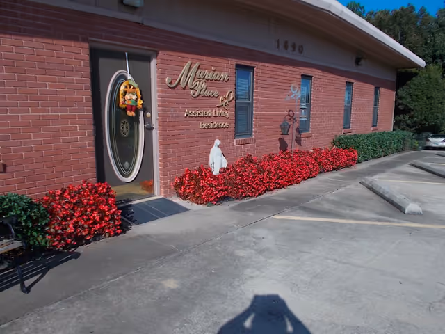 Brick Marian Place Assisted Living entrance with red flowering shrubs along walkway