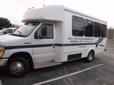 White shuttle bus with blue stripes parked in a lot, bearing facility text.