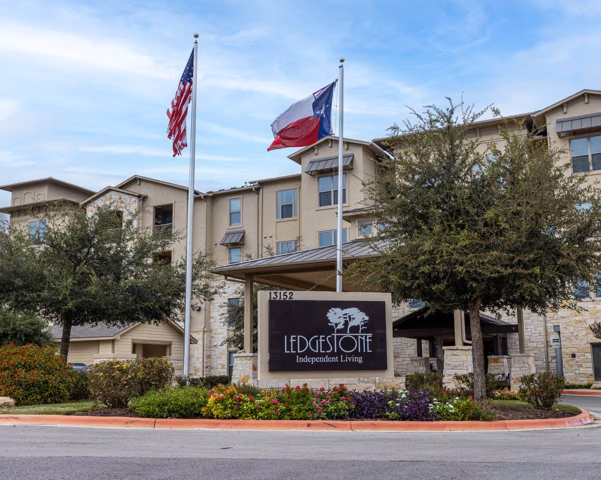 Exterior view of Ledgestone Independent Living building with flags and landscaped entrance.