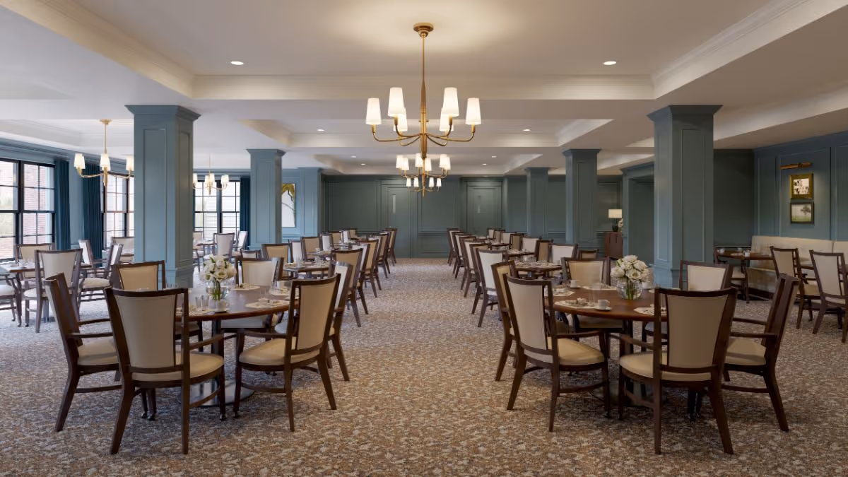 Spacious dining room with multiple round wooden tables and upholstered chairs, chandeliers, and large windows.
