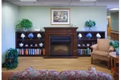 A cozy common area featuring a fireplace with a painting above, flanked by bookshelves with decorative items and books, and upholstered seating.