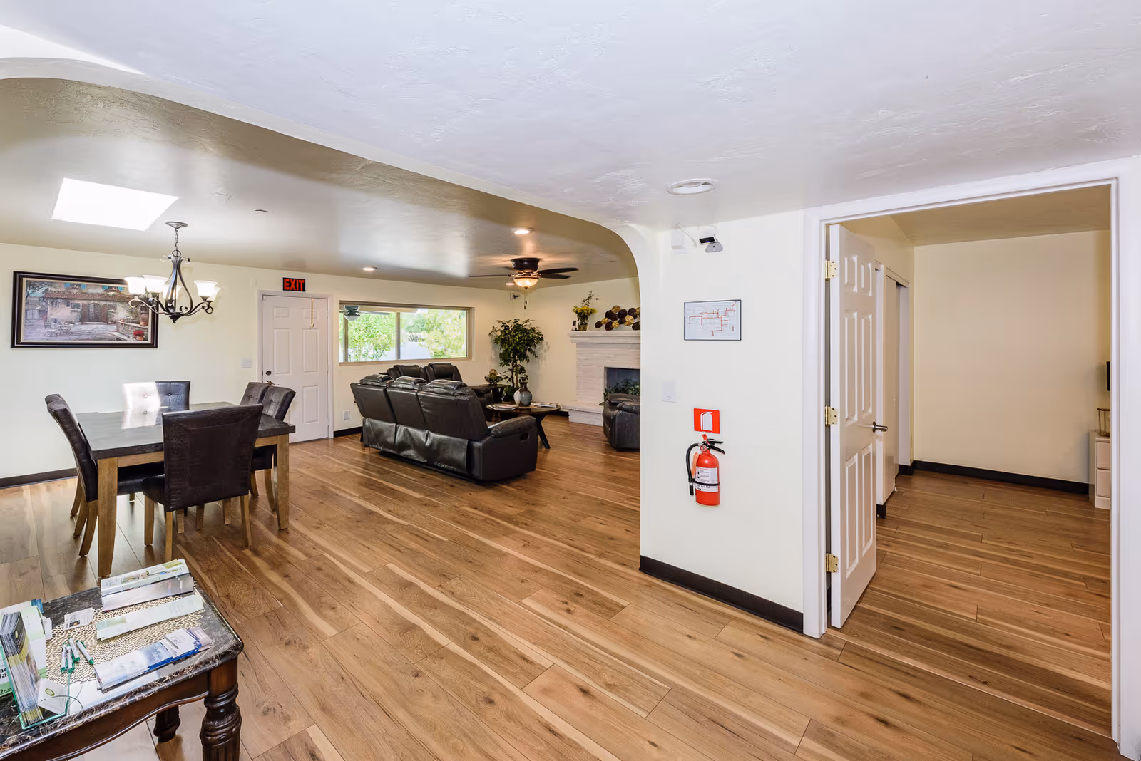Open common area with a dining table, leather sofas, fireplace and wood flooring in an assisted living facility.