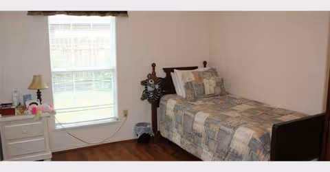 A bedroom with a single bed, patchwork quilt, nightstand, and a window.