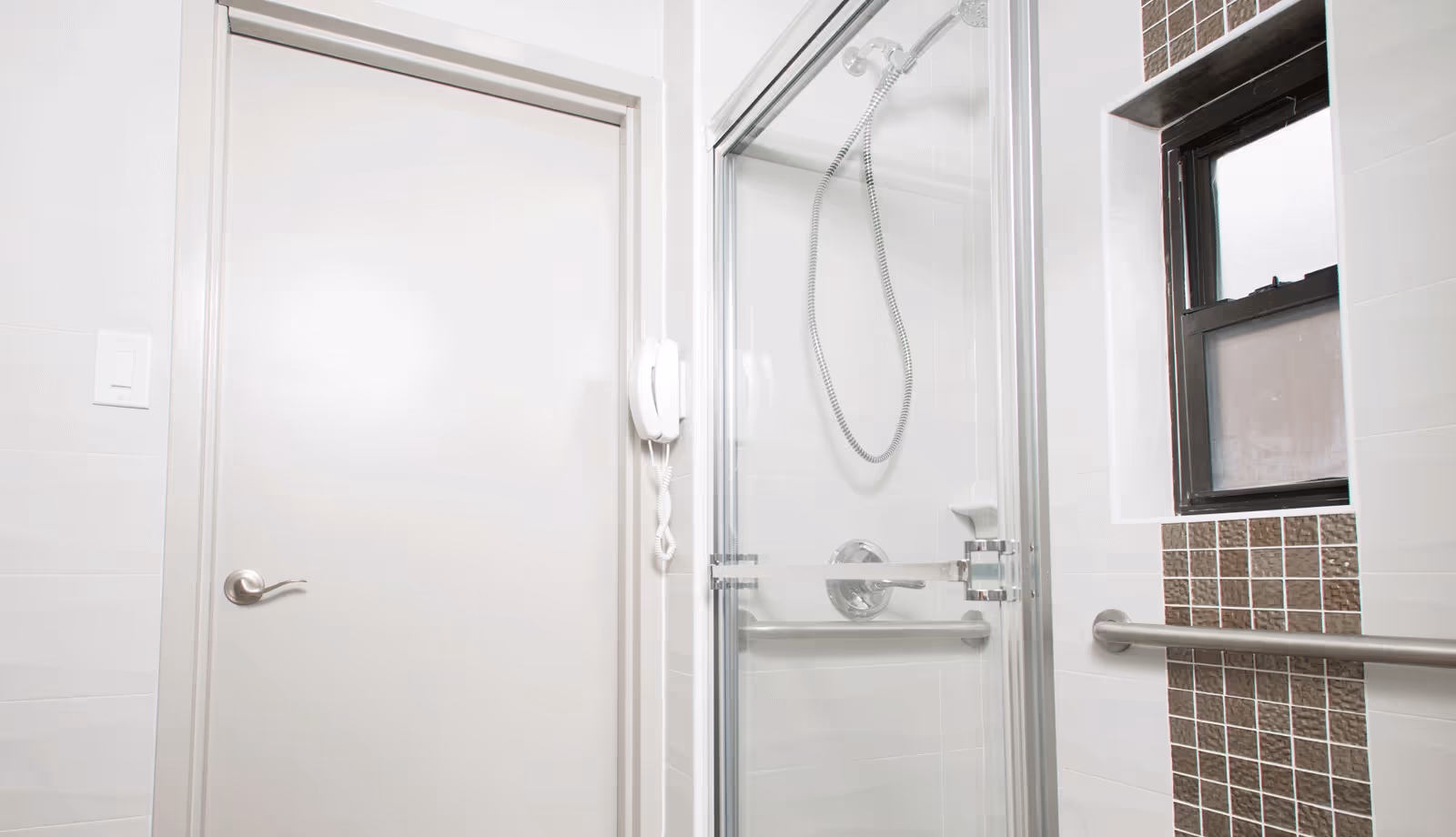 Bright accessible bathroom with a glass-enclosed shower, grab bars, tiled accent wall and a small window.