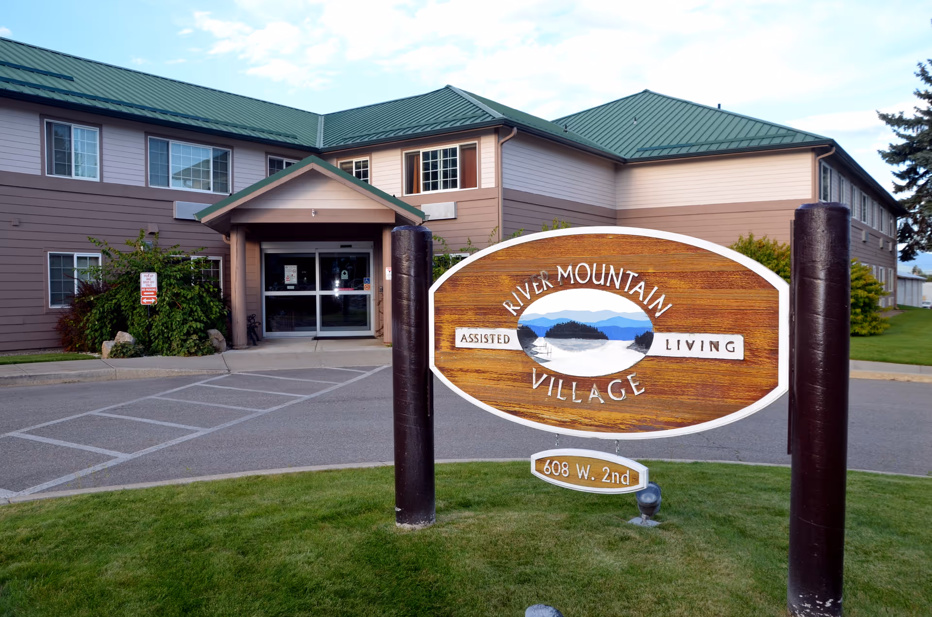 Entrance of River Mountain Village assisted living building with a wooden sign and driveway in front.