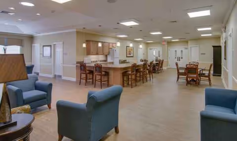 Spacious senior living common area with kitchenette, dining tables, and lounge chairs.