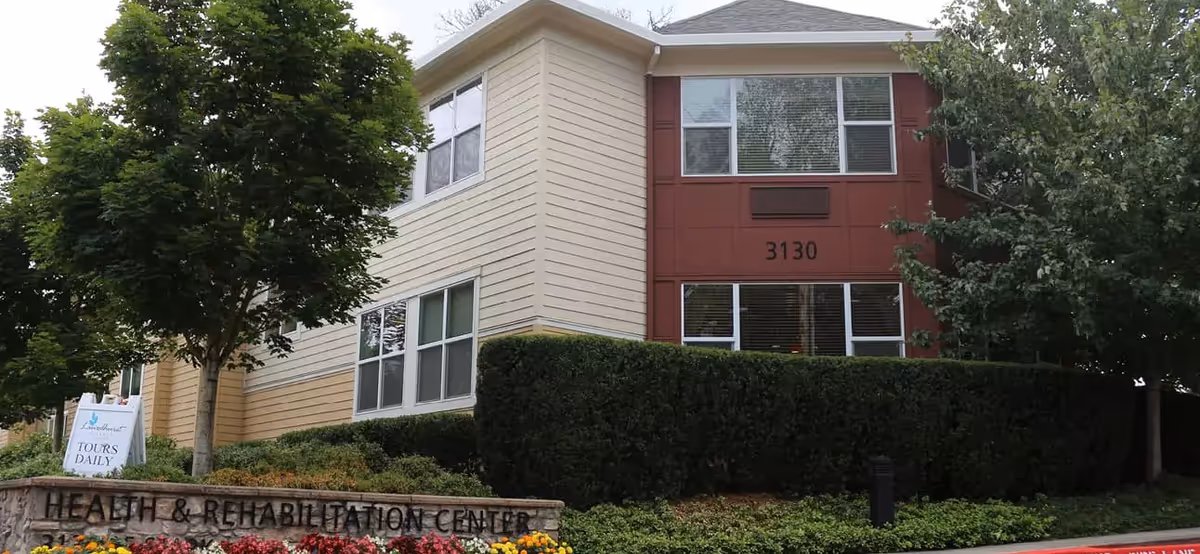 Front exterior of a two-story health and rehabilitation center (3130) with hedges, trees and a flowerbed.