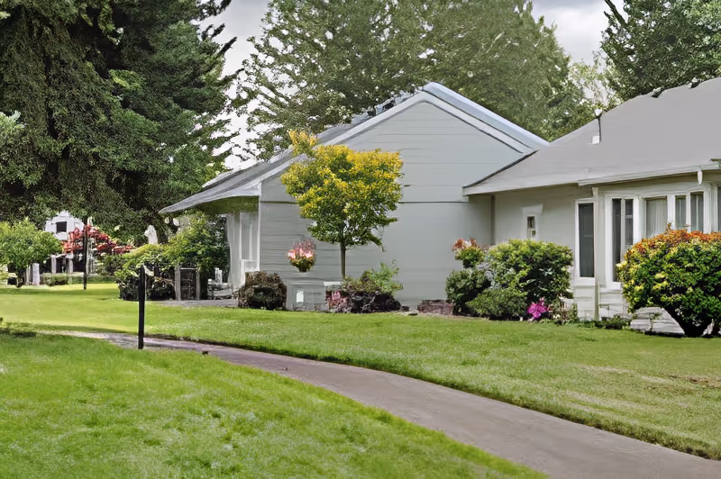 Light-gray single-story building surrounded by manicured lawn, shrubs, and a curved paved walkway.