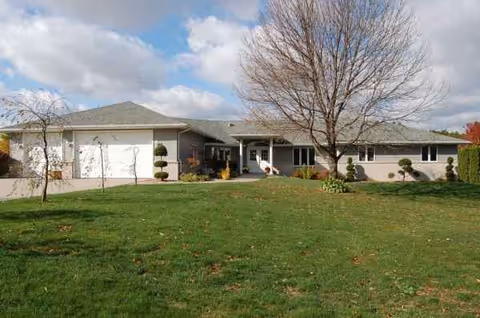 Single-story senior living facility with a manicured lawn, driveway, and bare trees.