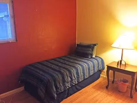 A small bedroom with a single bed, striped bedding, nightstand, and lamp.