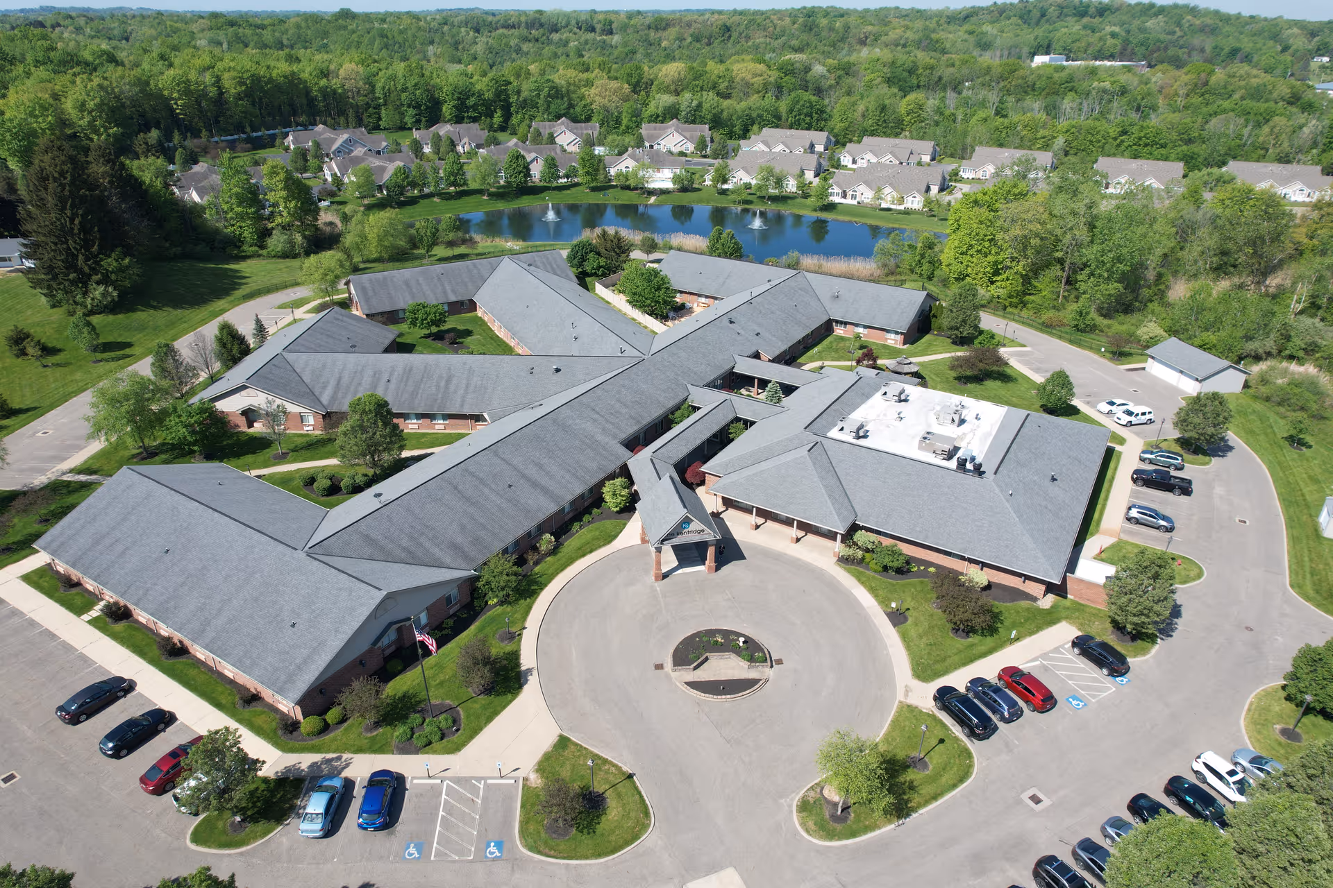 Aerial exterior view of The KentRidge Senior Living campus showing interconnected buildings, a circular driveway, parking lots, and a pond with fountains.