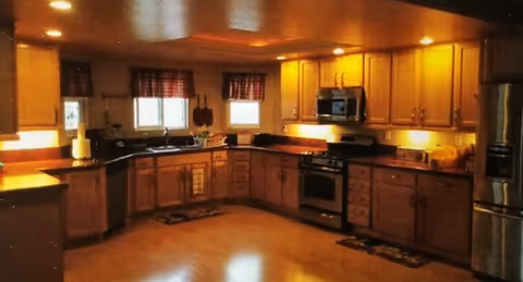 U-shaped kitchen with wooden cabinets, countertops, appliances, and three small windows.