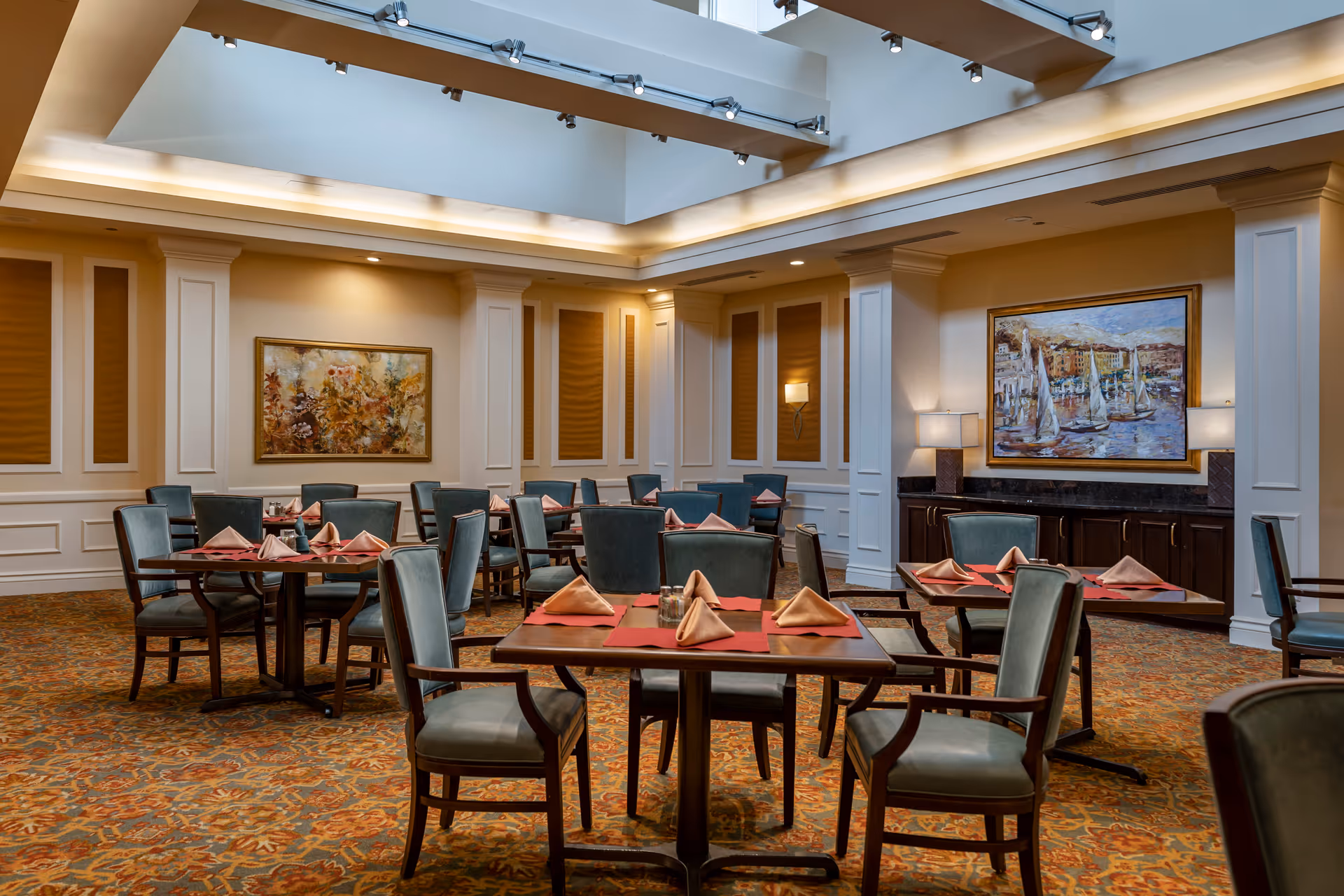 Dining room with multiple tables set with napkins and upholstered chairs beneath a skylight.