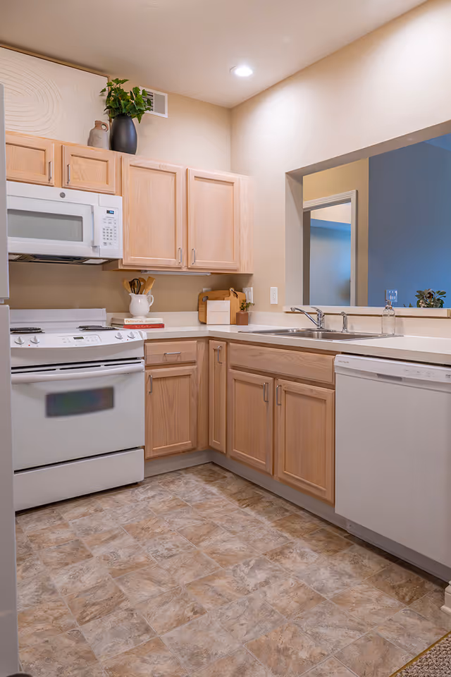 Small kitchen with light wood cabinets, white appliances, a double sink, and a tiled floor.
