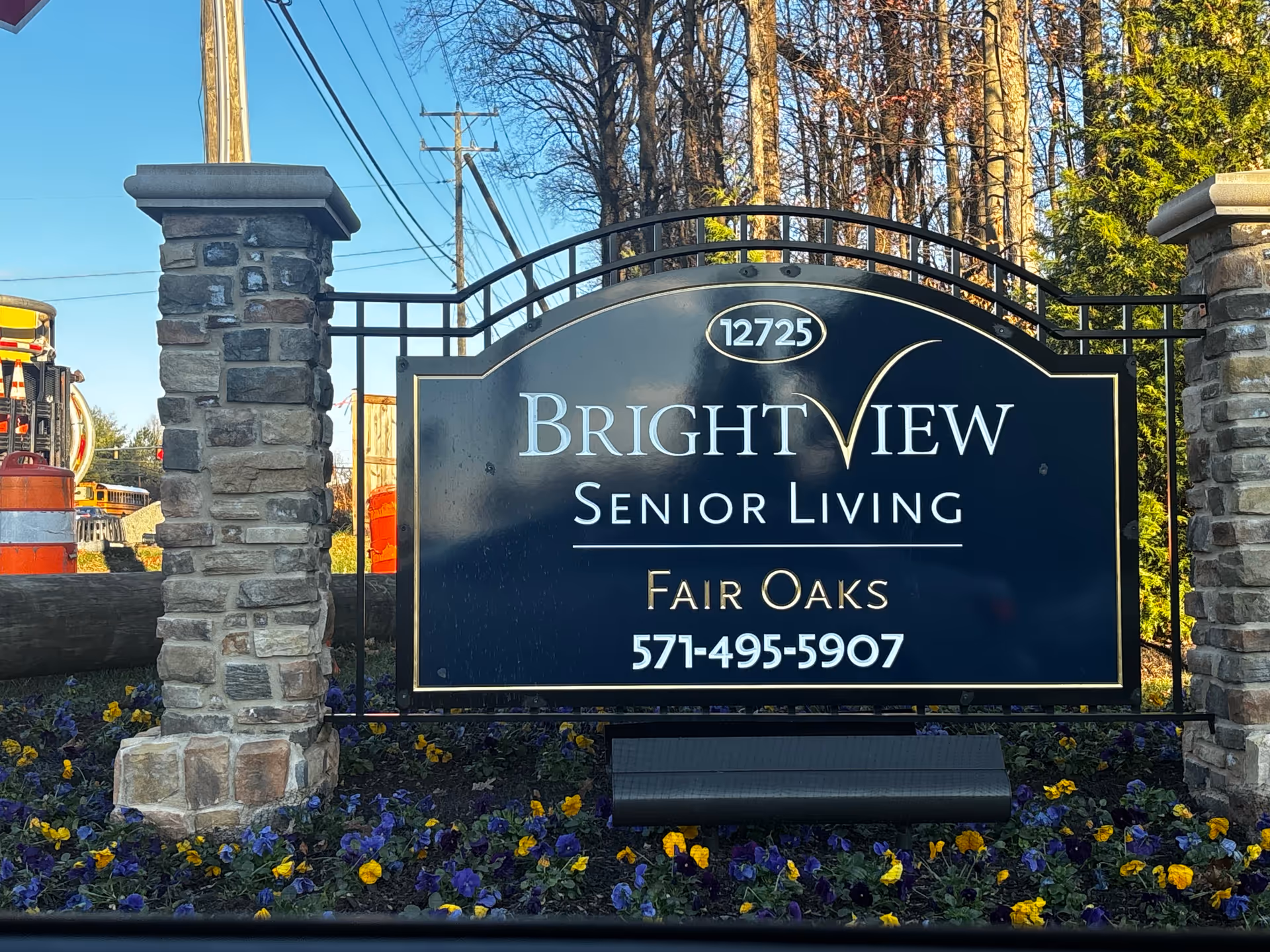 Entrance sign reading 'Brightview Senior Living Fair Oaks' with phone number mounted between two stone pillars and flowers at the base.