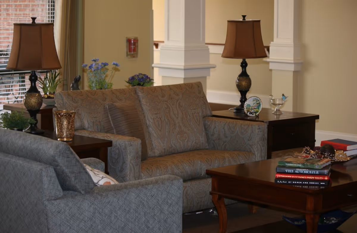 Cozy living room with patterned sofas, a wooden coffee table stacked with books and side tables topped with lamps and decorative accents.