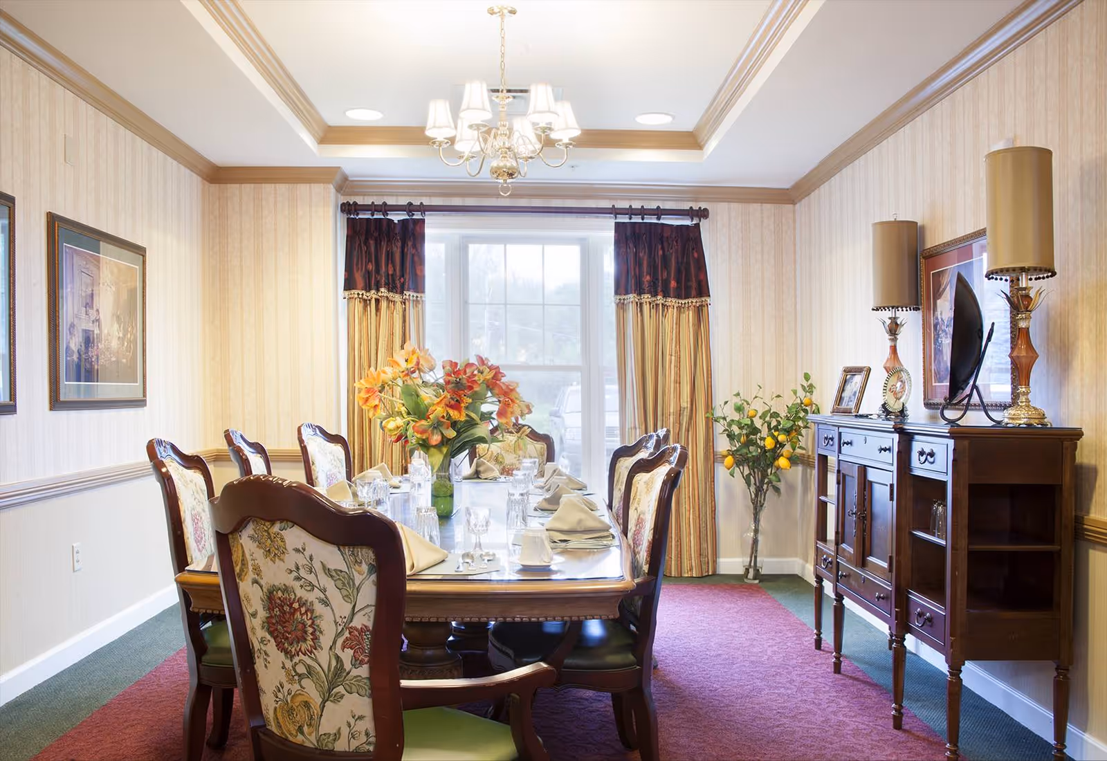 Formal dining room with a set table, upholstered chairs, chandelier, sideboard and a window with curtains.