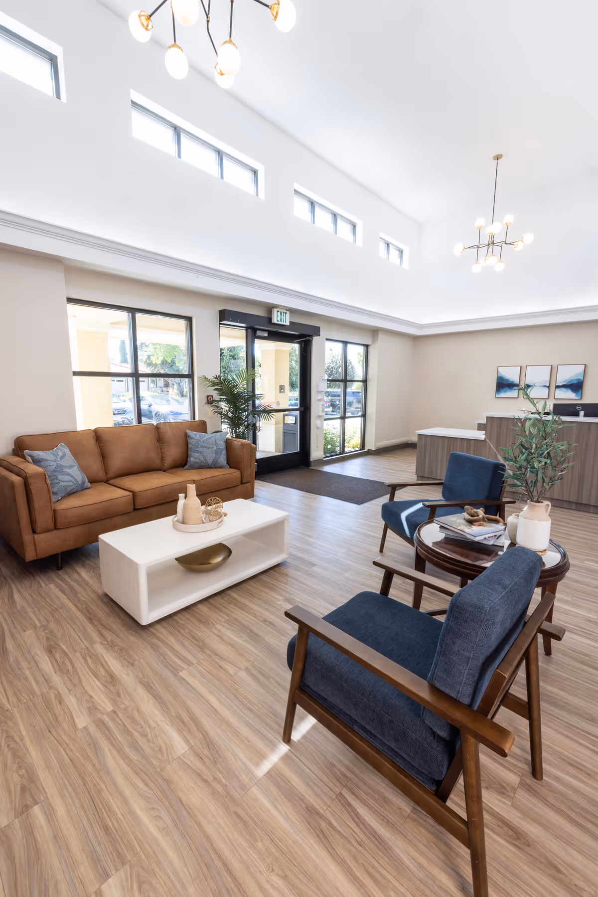 Bright modern lobby with a sofa, two armchairs, coffee tables, and a reception desk by the glass entrance.