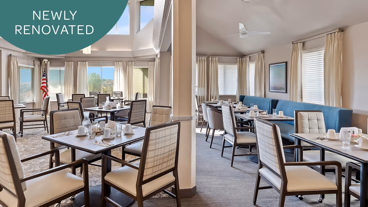 Bright, newly renovated dining room with multiple set tables and upholstered chairs and large windows.
