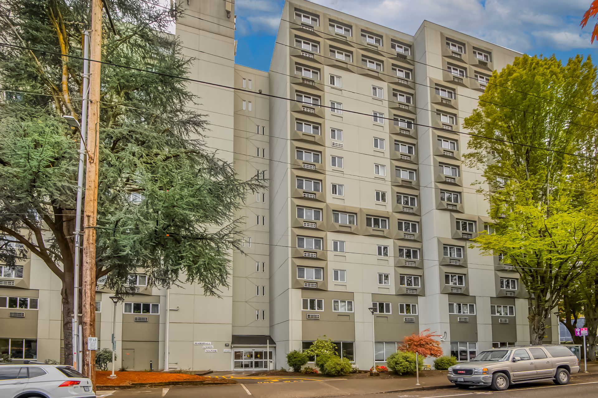 Exterior view of a multi-story senior living facility named Marshall Union Manor with several windows, surrounded by trees and parked cars in front.