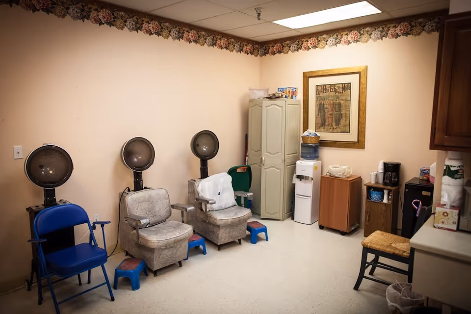 Small salon-style room with three vintage hooded hair dryers and chairs, a water cooler, cabinets and a coffee station.