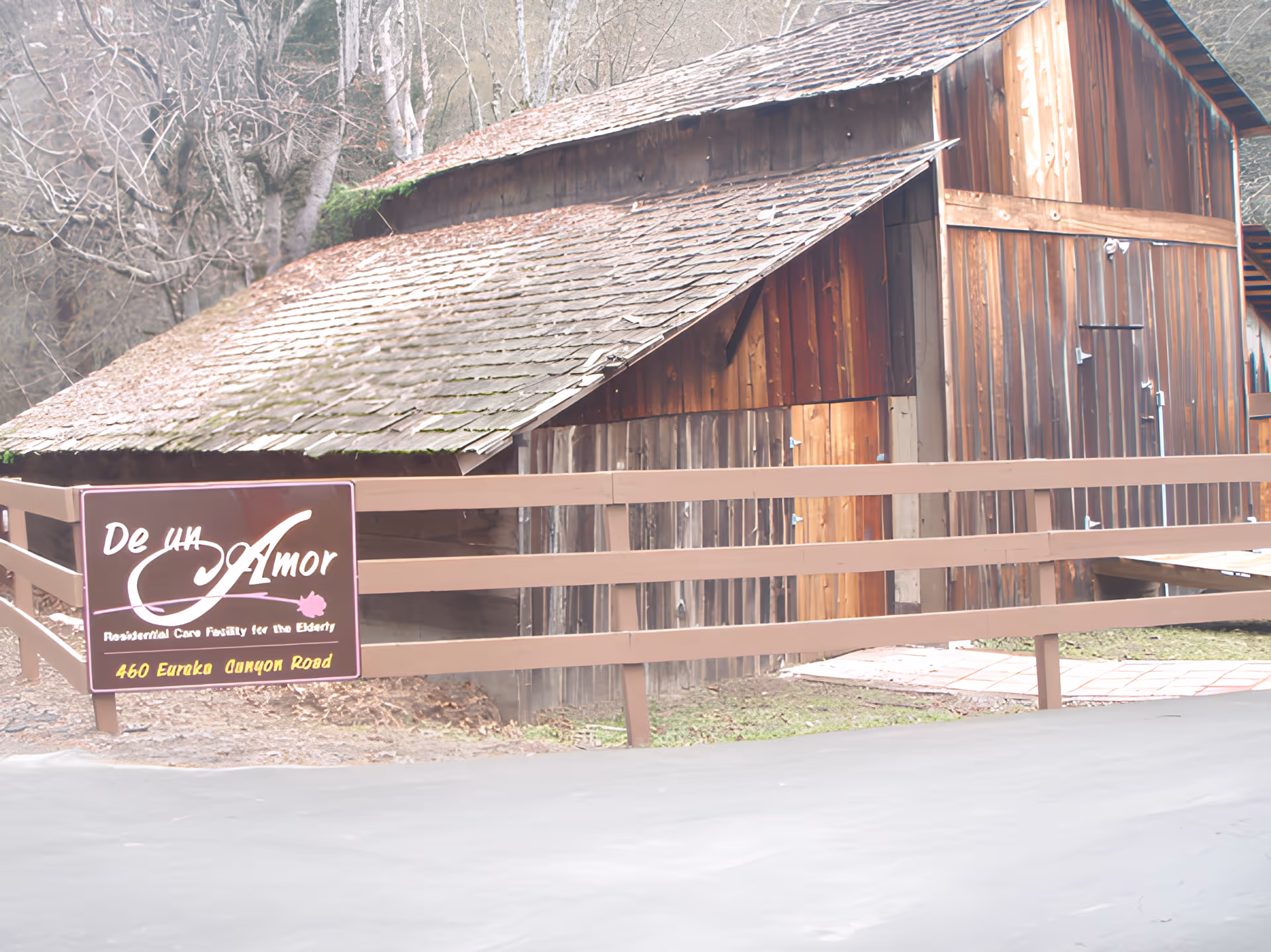 Rustic wooden building and fence with a 'De un Amor' sign for a residential care facility.