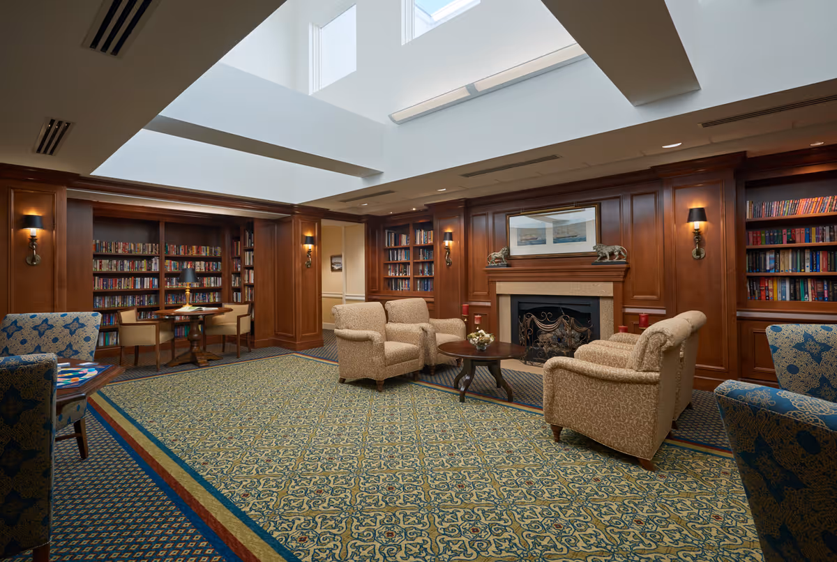 Library-style sitting room with wood-paneled bookshelves, a fireplace, and upholstered armchairs beneath a skylight.